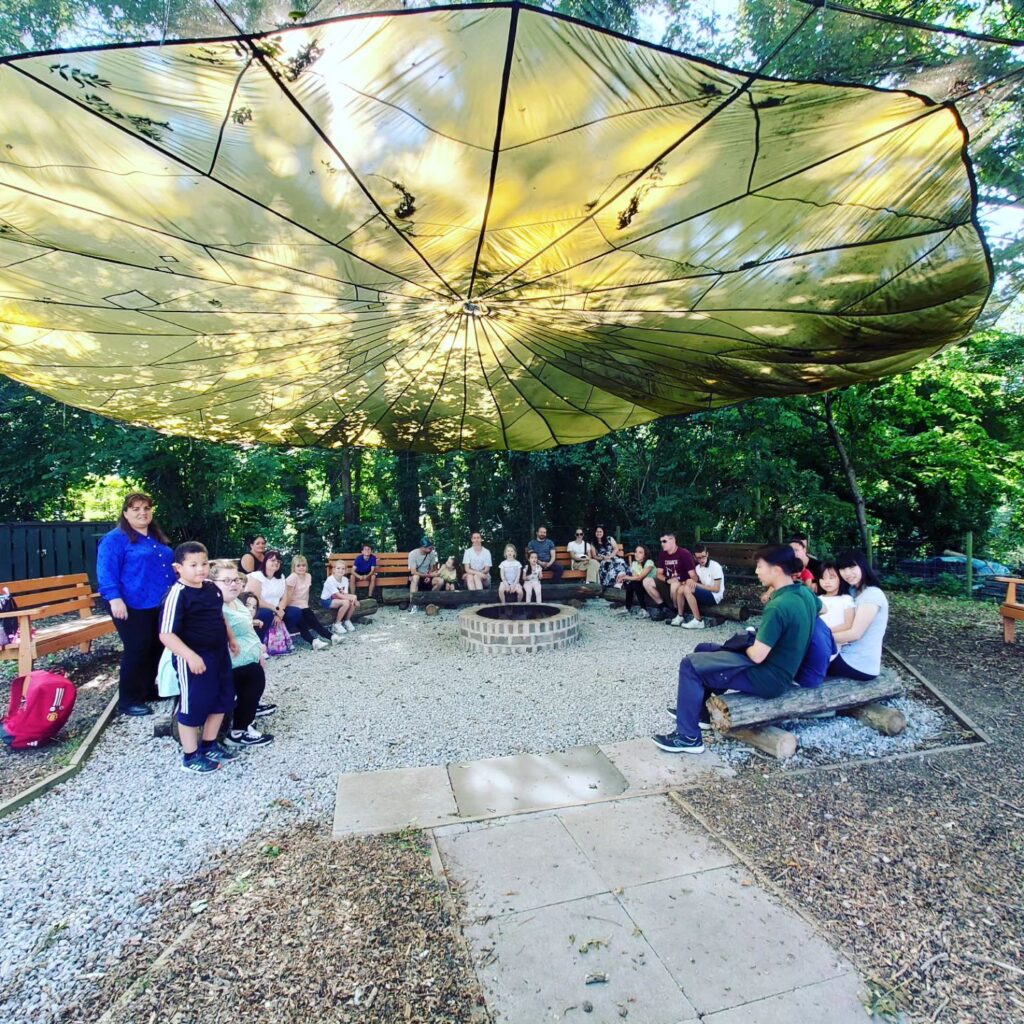 Group photo of families attending an event sitting underneath a cover outside around a campfire